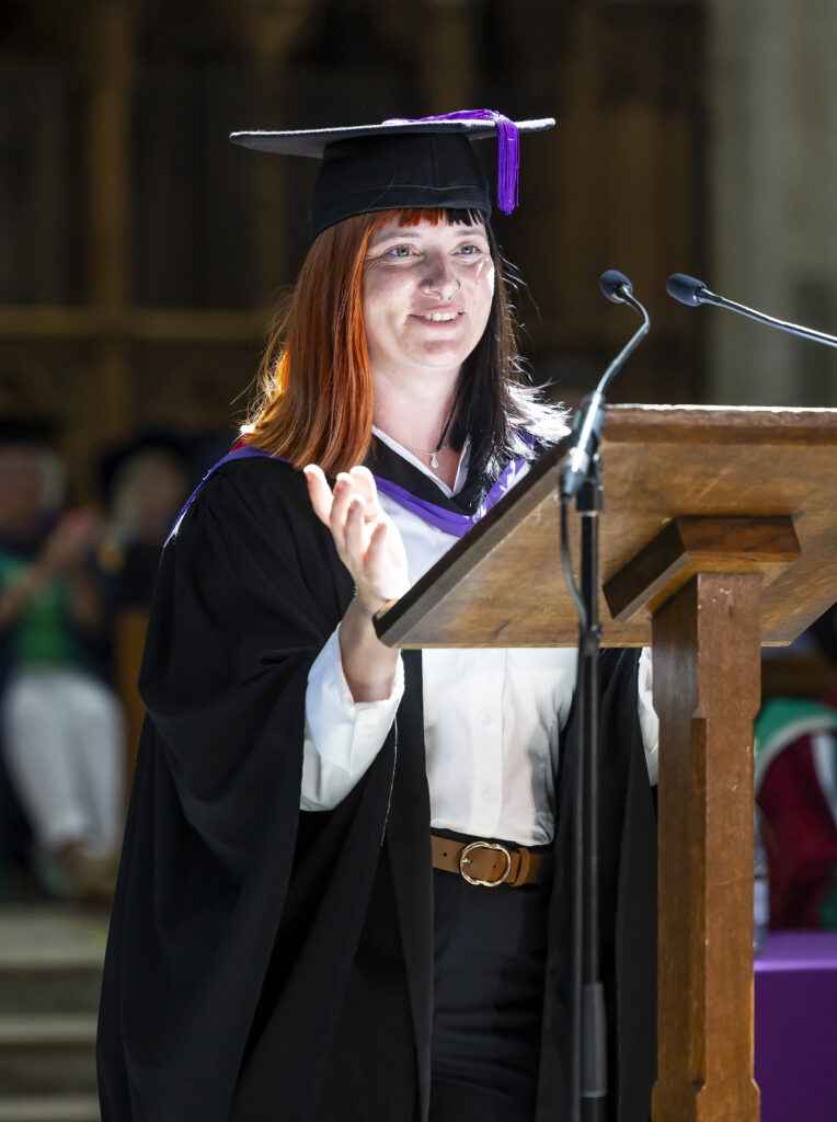 A student in a UCS graduate gown giving a speech