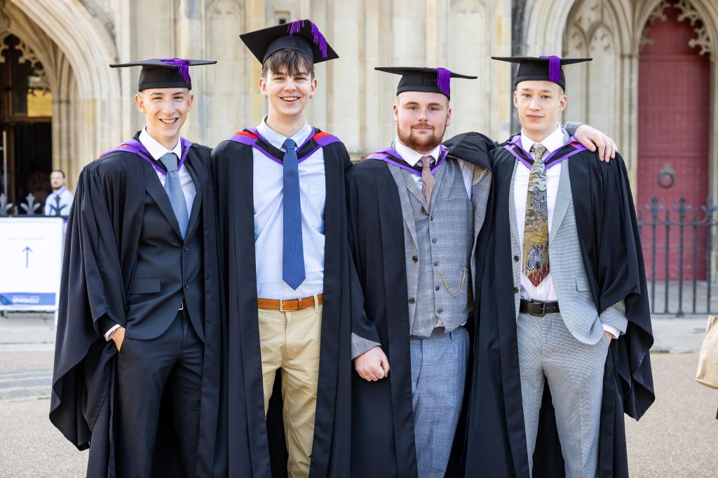 Four graduates in academic gowns and mortarboards standing together outside Winchester Cathedral during University Centre Sparsholt graduation