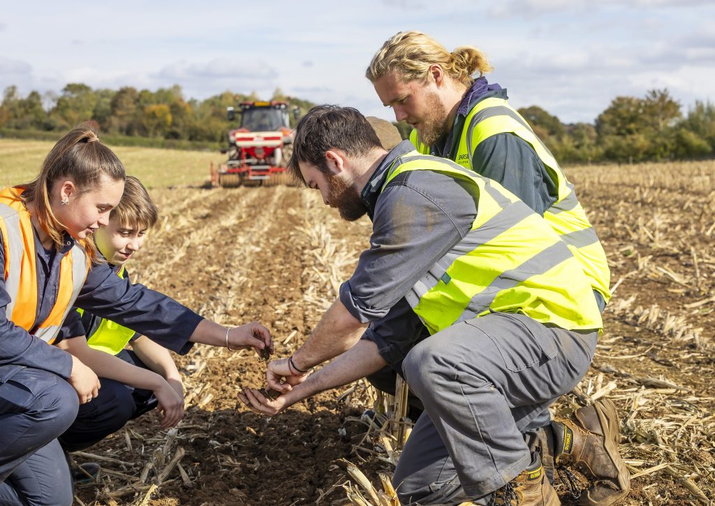 Agriculture students in high vis jackets in an agricultural field holding a handful of soil to assess quality
